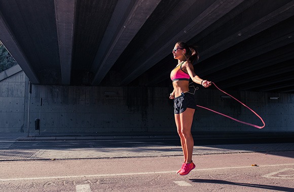Rope skipping – woman skipping using a pink rubber skipping rope. Rope skipping – woman skipping using a pink rubber skipping rope.