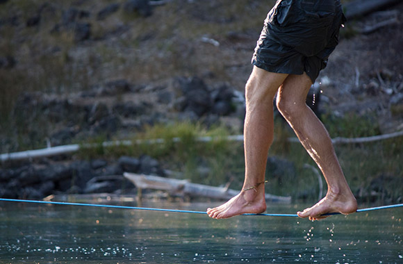 Slackline – Een man balanceert op een waterlijn boven het water.