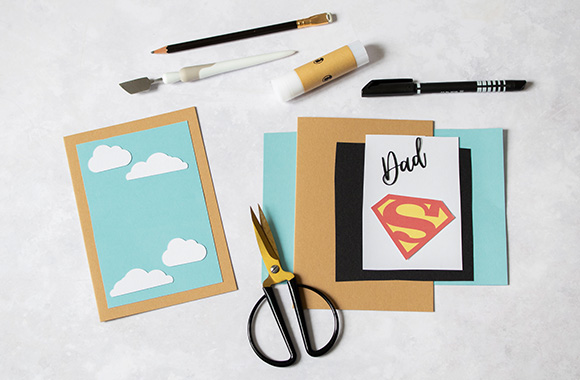 Materials for a Father's Day card with superhero logo.