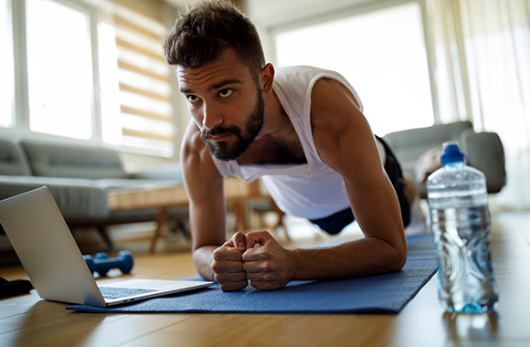 Online fitness: young man doing a plank with guidance from a fitness video.