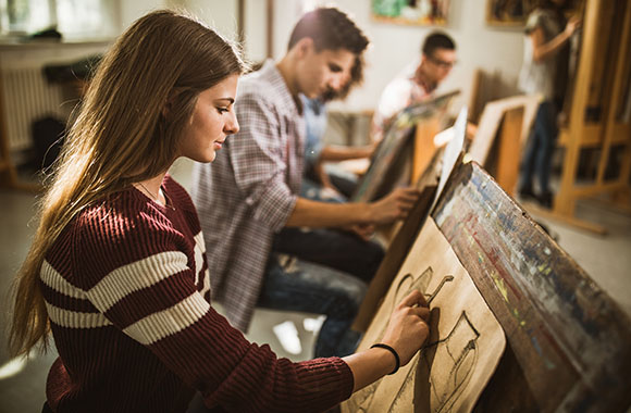 Young woman drawing a still life painting in an art class.