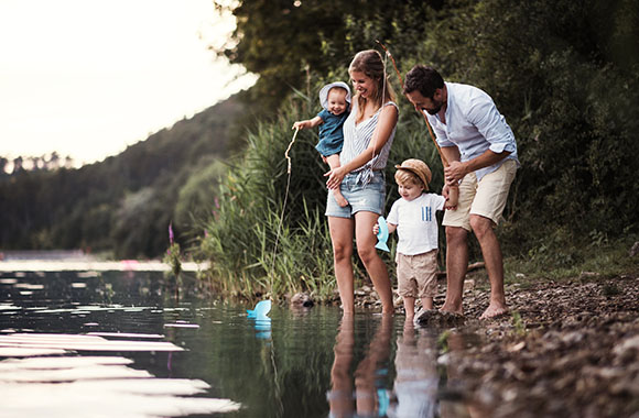 Attività all’aperto per bambini: famiglia esplora la riva di un fiume durante una gita in famiglia.