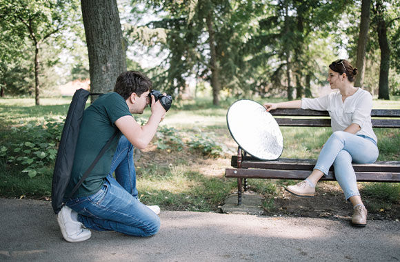 Cómo hacer buenos retratos fotográficos: un fotógrafo utiliza un reflector para hacer retratos en un parque.