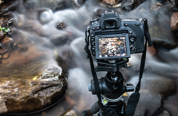 Shutter speed on a camera: a photographer taking a photo of a river with a long exposure time. Shutter speed on a camera: a photographer taking a photo of a river with a long exposure time.
