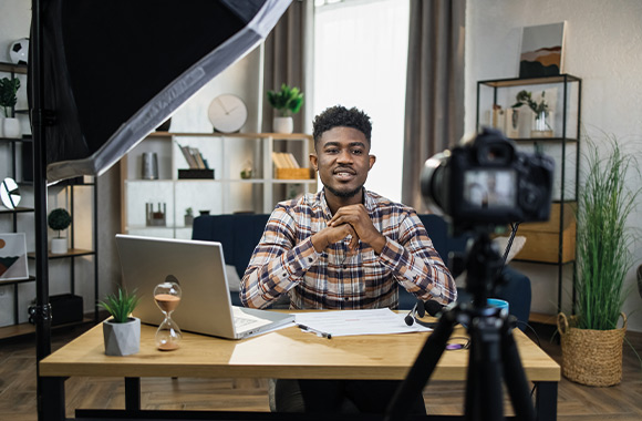 Making videos – a man sitting in front of a camera at his desk.