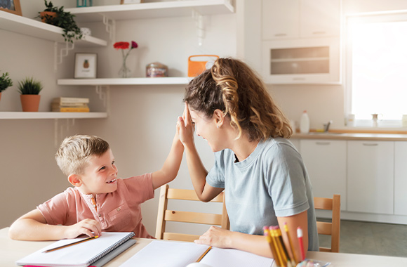 Come aiutare tuo figlio a fare i compiti: mamma e figlio battono il cinque dopo che il piccolo ha finito di fare i compiti.