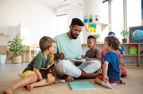 Erzieher schaut mit seiner Kindergartengruppe ein Bilderbuch an. Erzieher schaut mit seiner Kindergartengruppe ein Bilderbuch an.