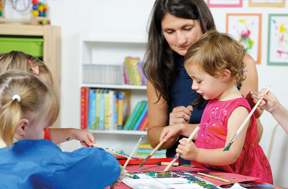 Péče o děti: děti v jeslích malují společně s vychovatelkou.