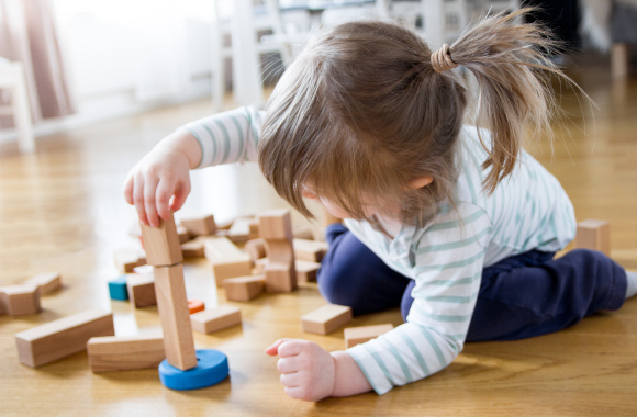 Gifts for toddlers: a little girl builds a tower out of wooden bricks.