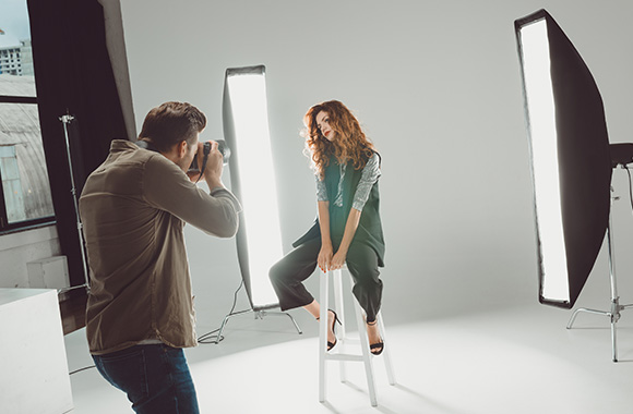 A fashion photographer doing a photoshoot with a model in a photo studio.