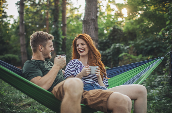 Eco-friendly holidays: holidaymakers relaxing in a hammock and drinking out of enamel mugs.