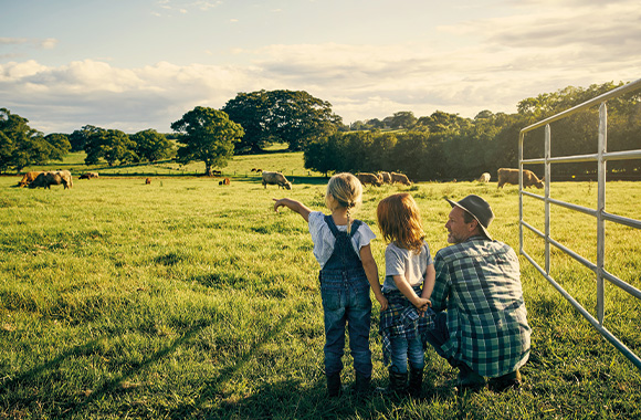 A father and his children on a farm looking at the cows in a field.