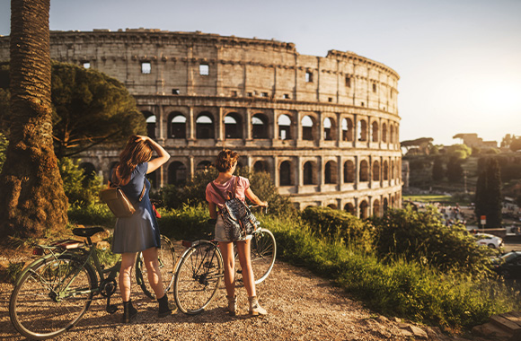 Sustainable holidays: two cyclists enjoying the view of the Colosseum in Rome.