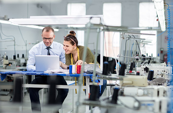 Clothing technology: two members of staff working in a textile factory on a laptop. Clothing technology: two members of staff working in a textile factory on a laptop.