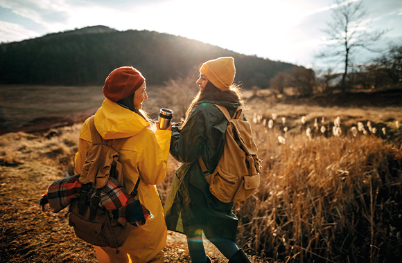 Minimalist travel tips: two holidaymakers carrying a rucksack and eco-friendly water bottles.