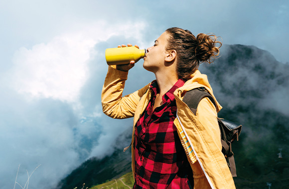 Sustainable holidays: a woman drinking out of a stainless steel water bottle.