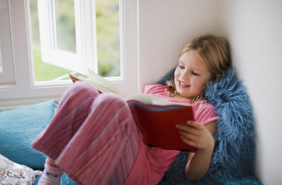 Gift 6-year-old: little girl sitting by a window reading a book.