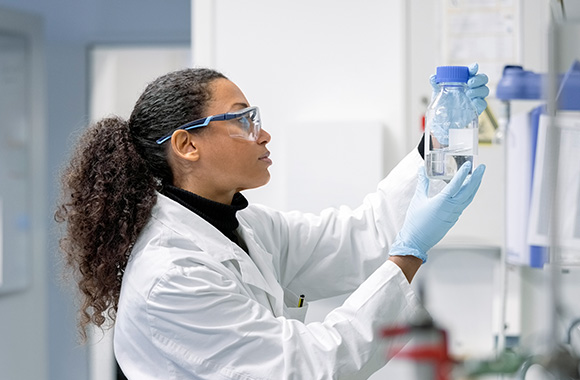 A young laboratory technician wearing safety goggles looking  at a solution  in the laboratory.