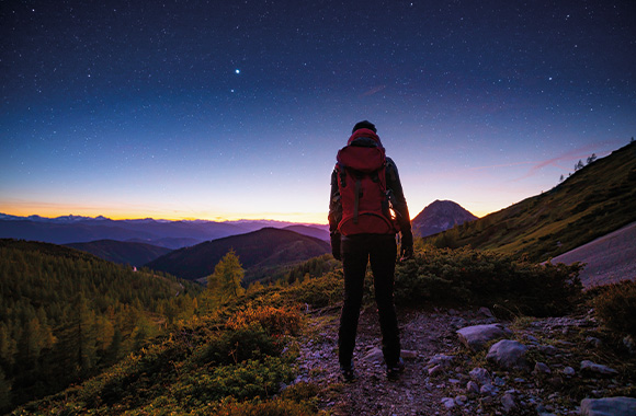 Mikroabenteuer erleben: Wanderer blickt während der blauen Stunde in die Ferne. Mikroabenteuer erleben: Wanderer blickt während der blauen Stunde in die Ferne.