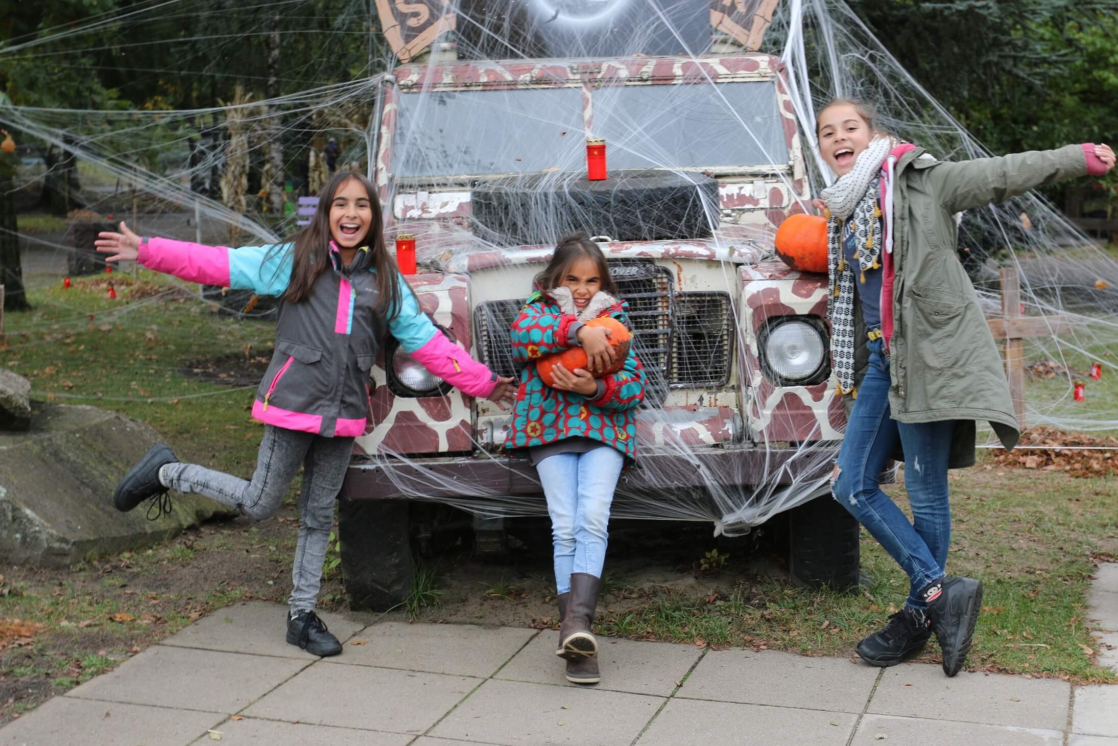 Kinder posieren mit Kürbissen vor einem für Halloween geschmückten Auto