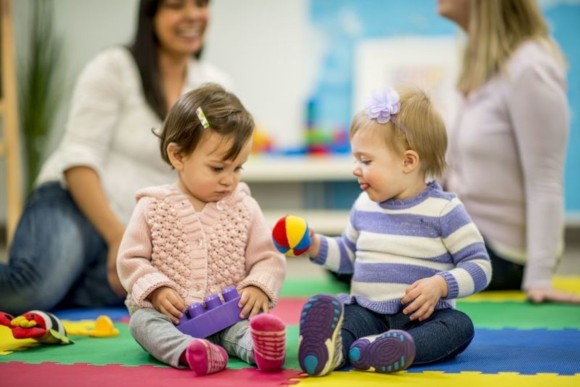 Kleinkinder spielen in der Spielegruppe, während sich die Mütter unterhalten Kleinkinder spielen in der Spielegruppe, während sich die Mütter unterhalten