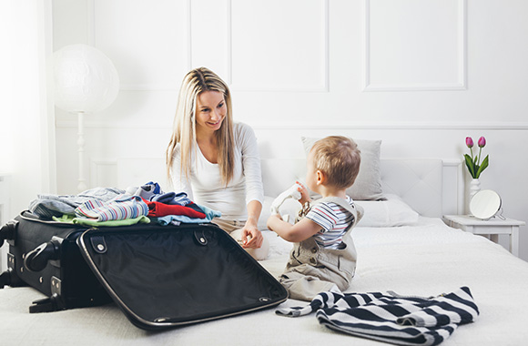 Kleines Kind schaut Mutter beim Kofferpacken zu