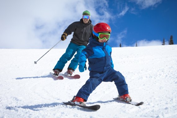 Kleiner Junge und Vater in Skiausrüstung fahren Piste hinunter