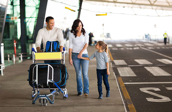 Kilkuletnia dziewczynka z rodzicami i wózkiem bagażowym na lotnisku