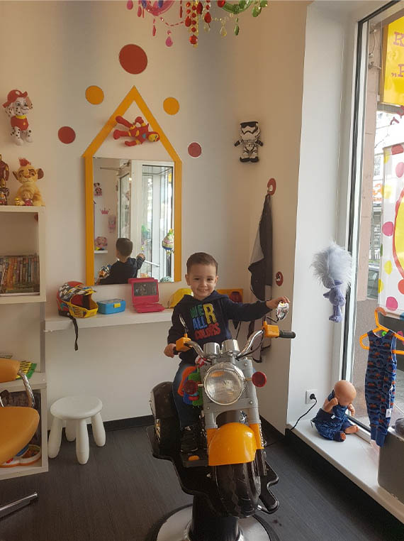 Junge auf einem Kinderfrisierstuhl als Motorrad Junge auf einem Kinderfrisierstuhl als Motorrad