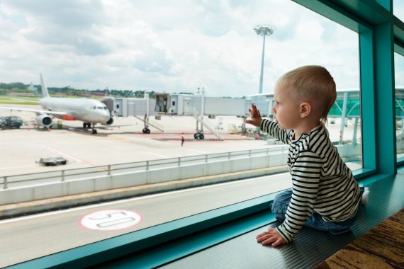 Kleiner Junge beobachtet durchs Fenster die Flugzeuge auf der Landebahn