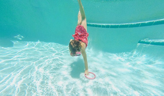 Une jeune fille plonge dans la piscine pour récupérer un objet Une jeune fille plonge dans la piscine pour récupérer un objet