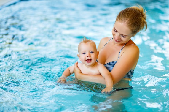 Een vrolijke baby wordt door zijn moeder in het zwembad vastgehouden. Een vrolijke baby wordt door zijn moeder in het zwembad vastgehouden.