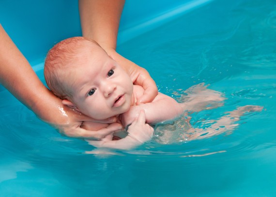 De baby zwemt in het water en wordt door de moeder met een speciale greep vastgehouden De baby zwemt in het water en wordt door de moeder met een speciale greep vastgehouden