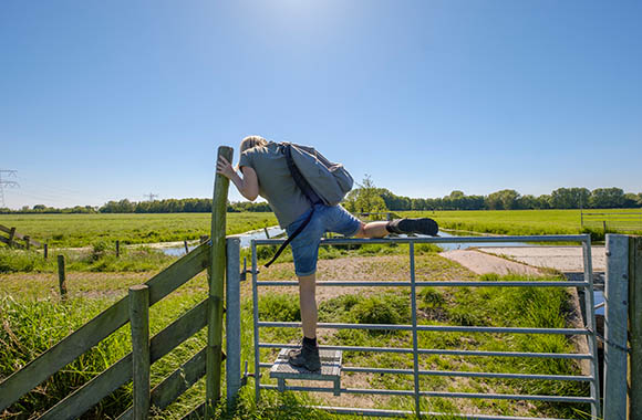 Juiste uitrusting voor een wandeling - vrouw met wandelschoenen en rugzak klimt over een hekje Juiste uitrusting voor een wandeling - vrouw met wandelschoenen en rugzak klimt over een hekje